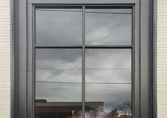 A large, four-pane window with a black frame, set into a light-colored brick wall, reflecting the cloudy sky.