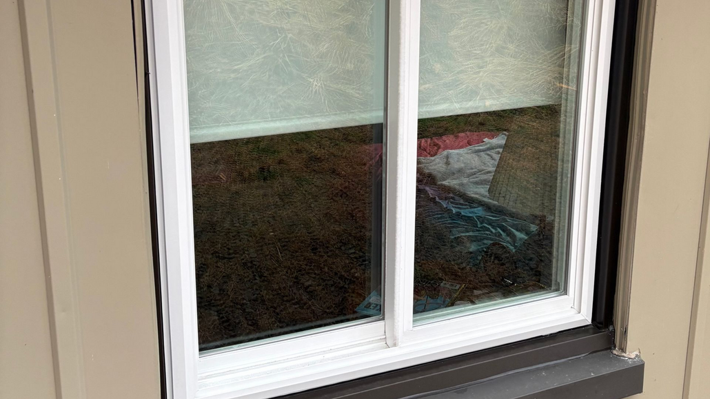 A view through a diamond-paned window; the left panes are fogged, while the right panes look out onto a lush green garden.