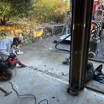 A man is kneeling down in a garage using a drill.