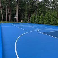 A blue basketball court with a basketball hoop in the middle of a forest.