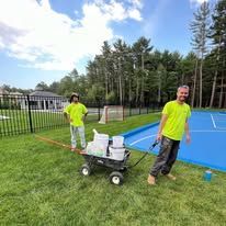 Two men are painting a tennis court with a wagon full of paint.