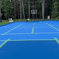 A man is working on a blue tennis court with a basketball hoop.