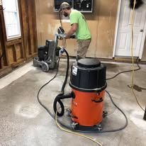 A man is using a vacuum cleaner to clean a concrete floor in a garage.