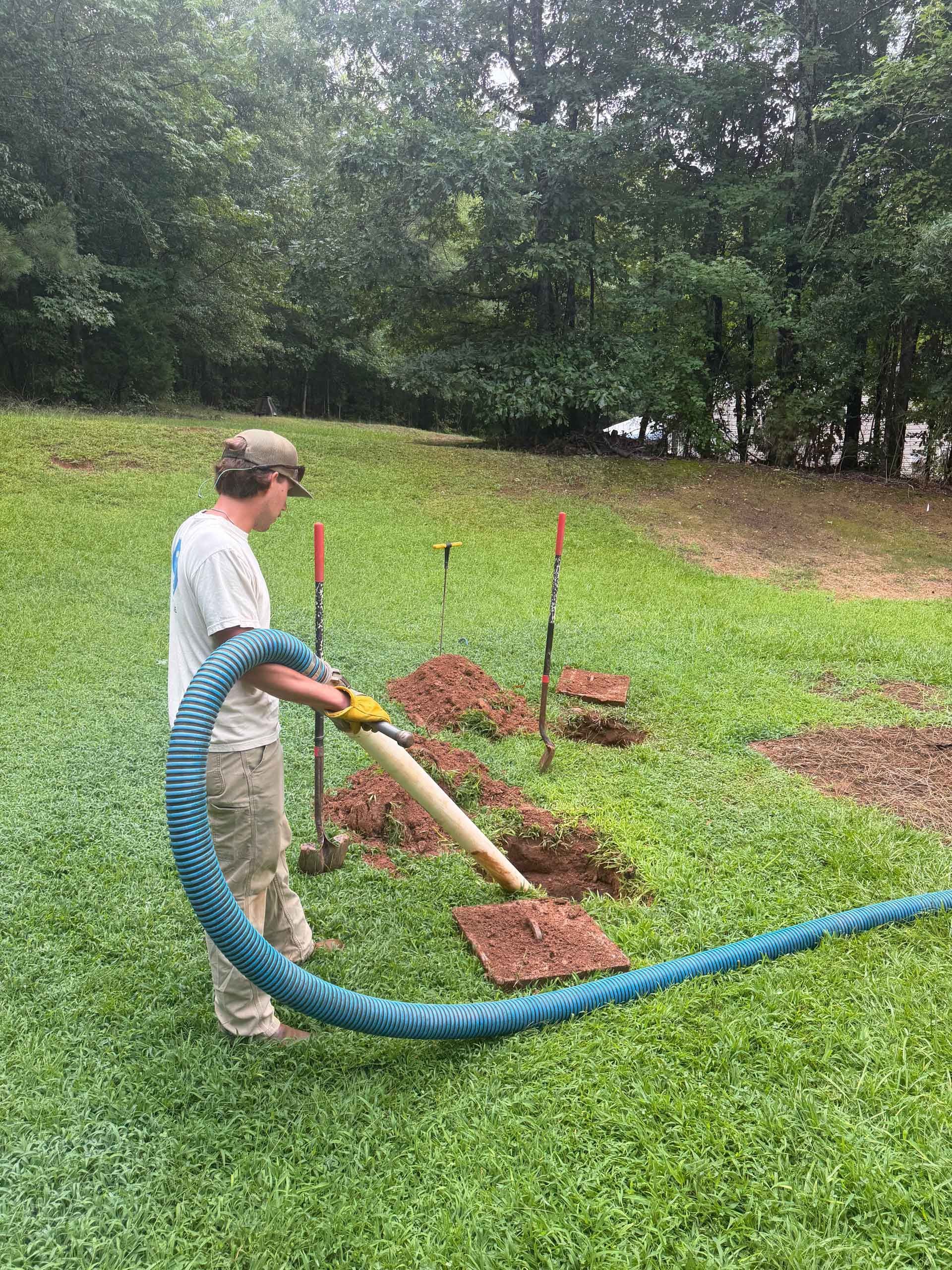 Person using a blue hose to mulch around young trees in a grassy yard