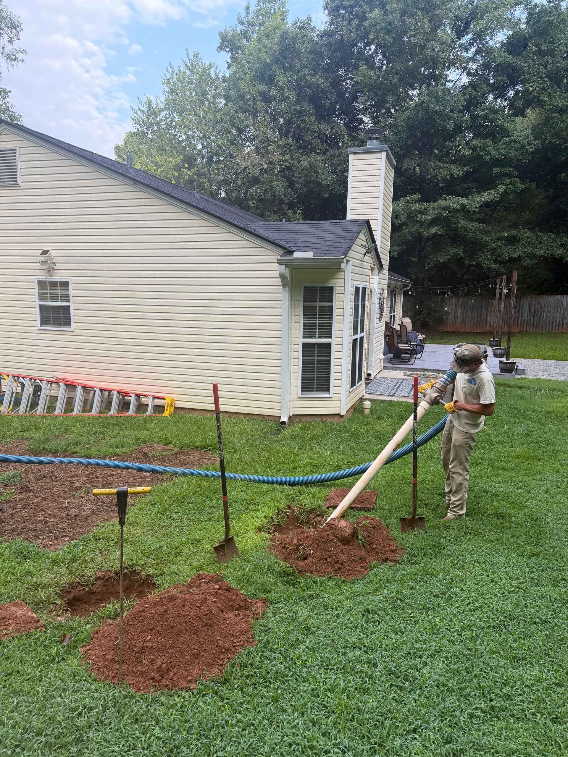 Worker on ladder near house exterior, installing small fence posts in a grassy yard.