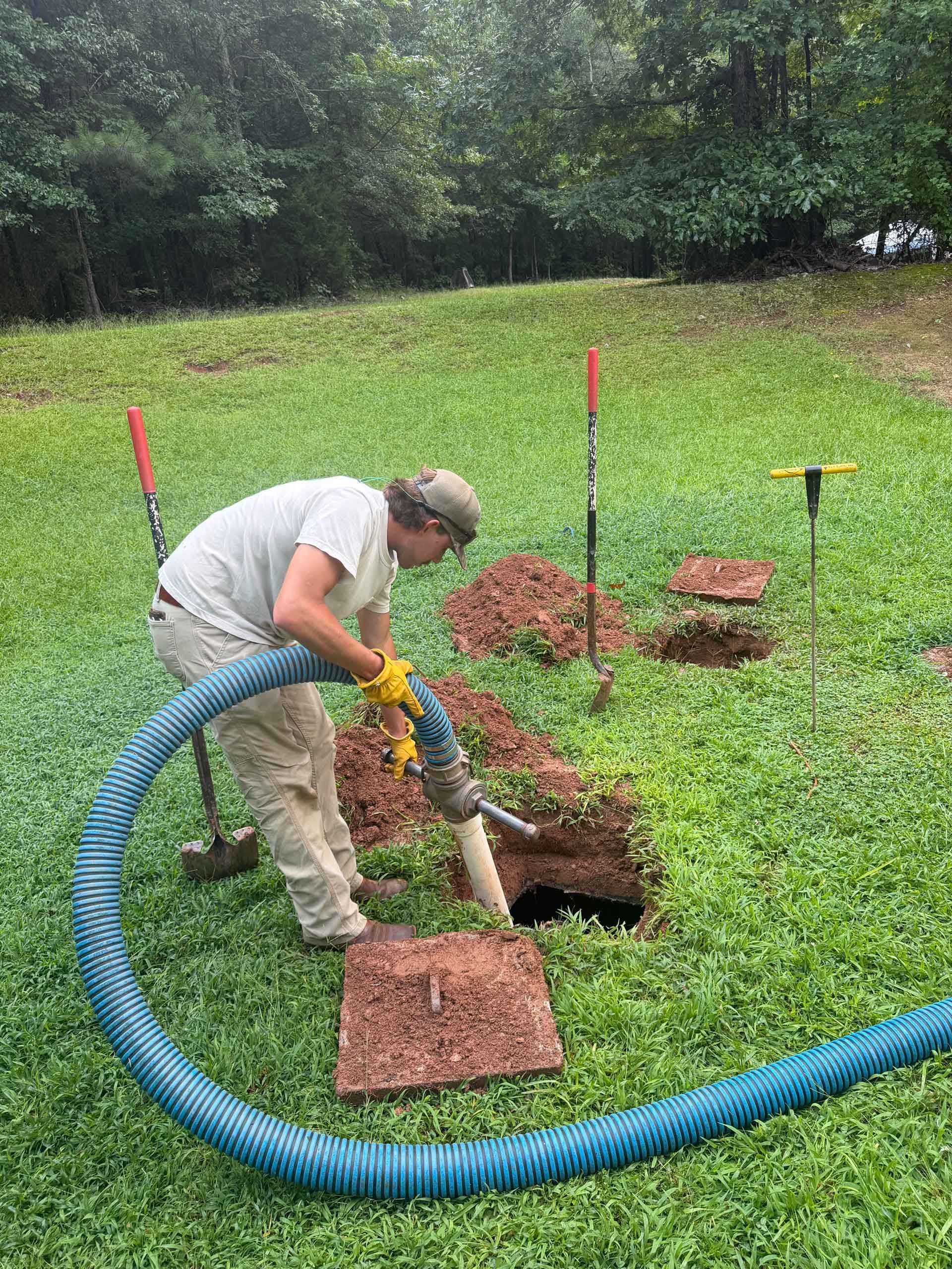 Person using a shovel beside a blue hose, digging a hole in a grassy yard.