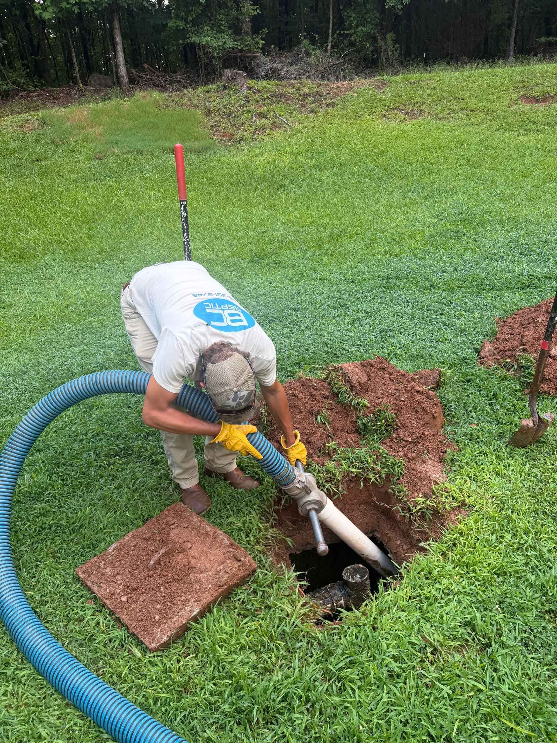 Worker using a pump to drain water from a grassy lawn hole with a hose nearby