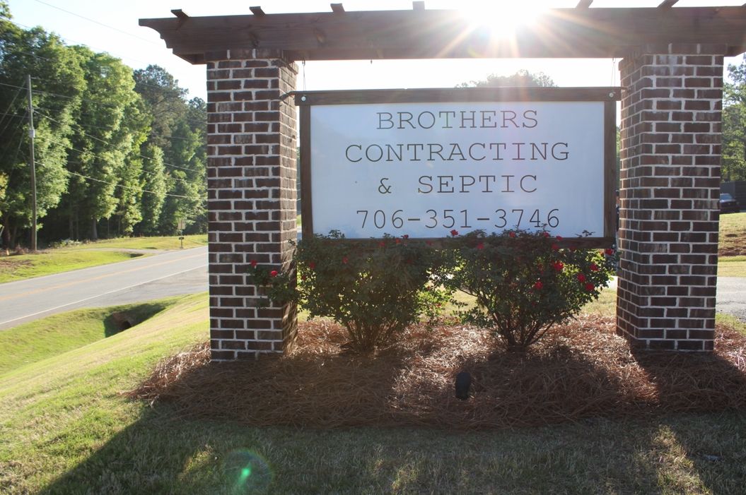 Brick entrance sign for Brothers Construction & Septic beside a roadside, with grass and trees around it