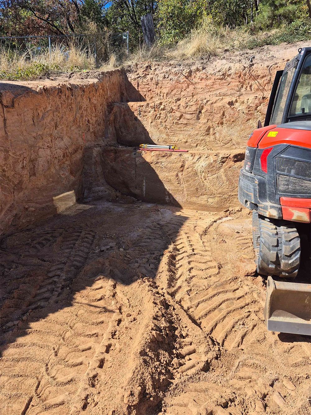 Excavator in an earthen construction site with cut away ground and tire tracks.