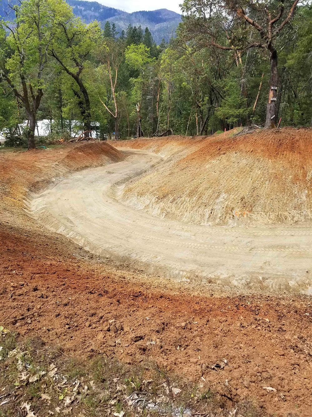Dirt bike track with brown soil and curved path, trees in the background.