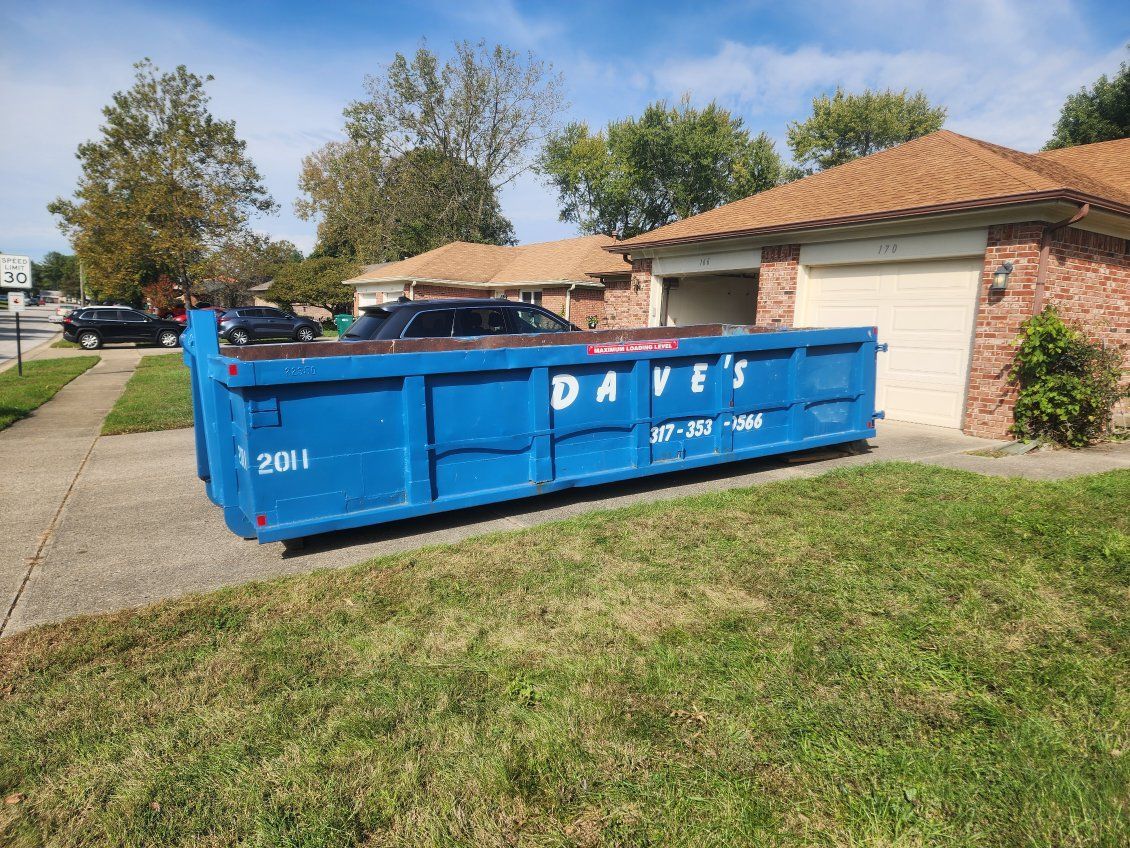 A blue dumpster is parked in front of a house.