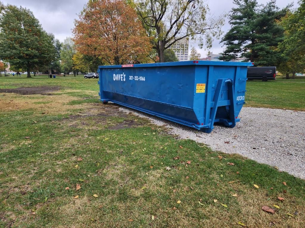 A blue dumpster is sitting in the middle of a grassy field.