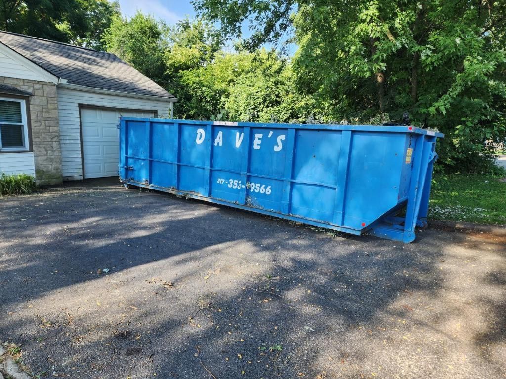 A large blue dumpster is parked in front of a house.