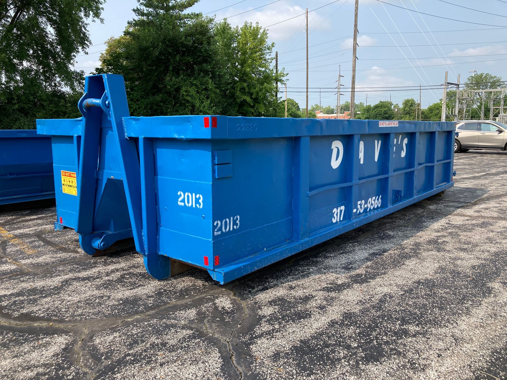A large blue dumpster is parked in a parking lot.