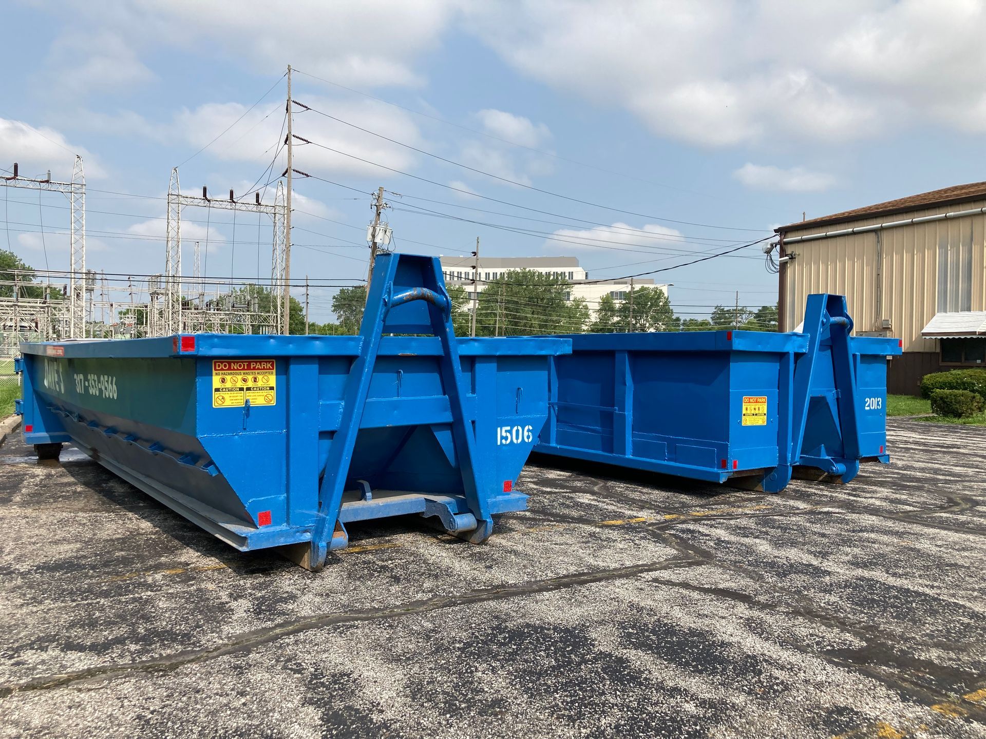 Two blue dumpsters are parked in a parking lot in front of a building.