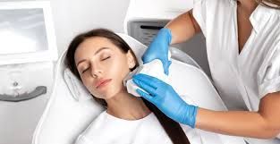 Woman receiving cosmetic treatment on her neck; technician using device, in a clinic setting.