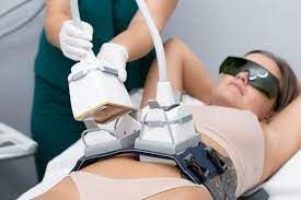 Woman undergoing body contouring treatment on her abdomen; technician uses applicators.