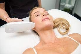 Woman receiving facial treatment, lying on a table with a device near her cheek.