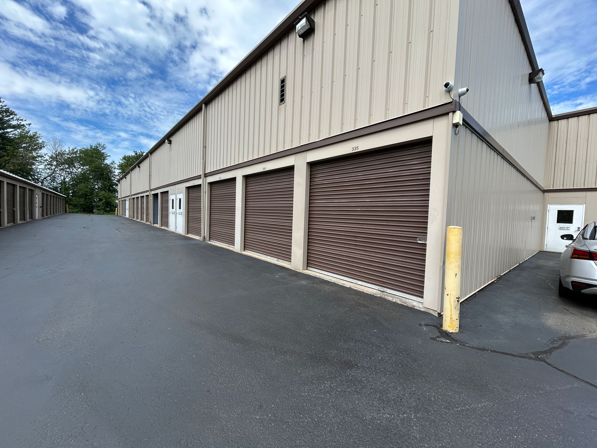 Row of brown storage unit doors beside a beige warehouse building on a paved lot