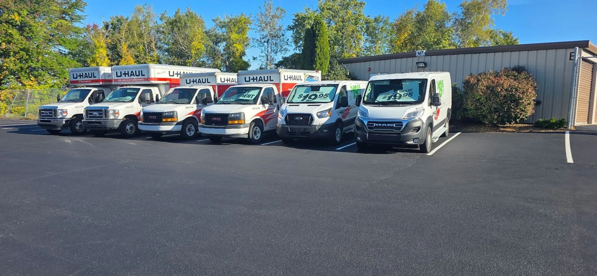 Line of parked service vans and trucks in a lot beside a warehouse on a sunny day