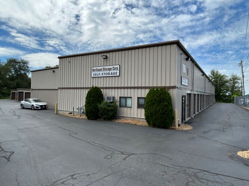 Tan industrial warehouse building with a parked white car and cloudy sky overhead