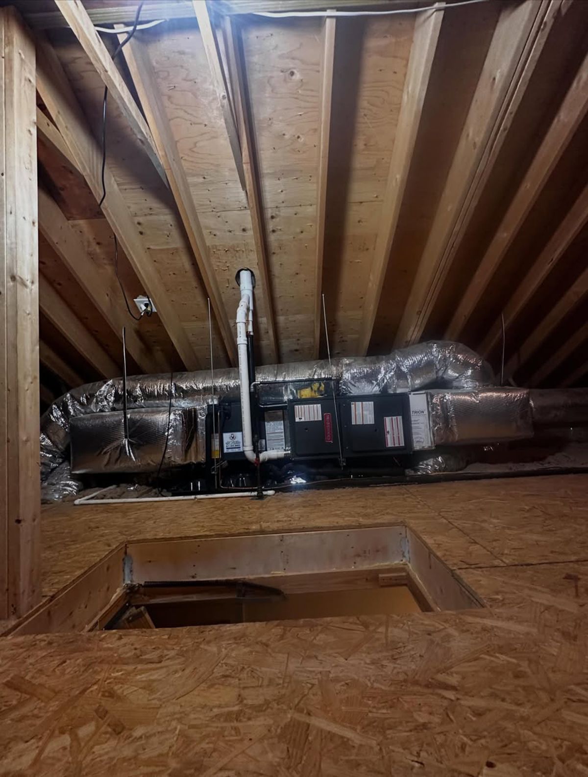 Exposed attic with insulated HVAC ductwork and furnace above a ceiling opening