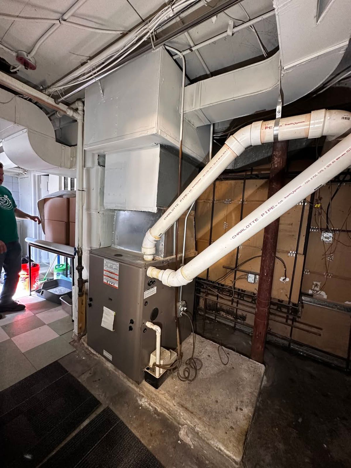 HVAC equipment and white ductwork in a utility room, with exposed ceiling and cardboard storage in back