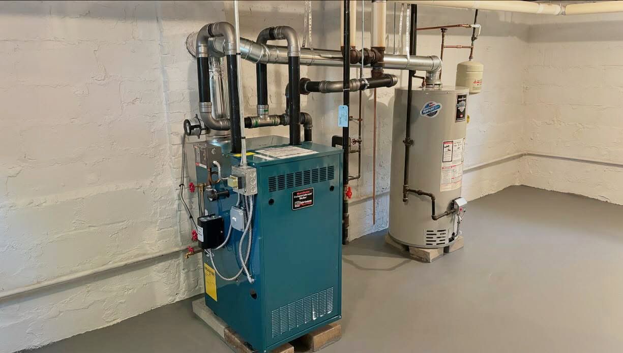 Blue industrial boiler and piping system in a utility room with white walls and concrete floor