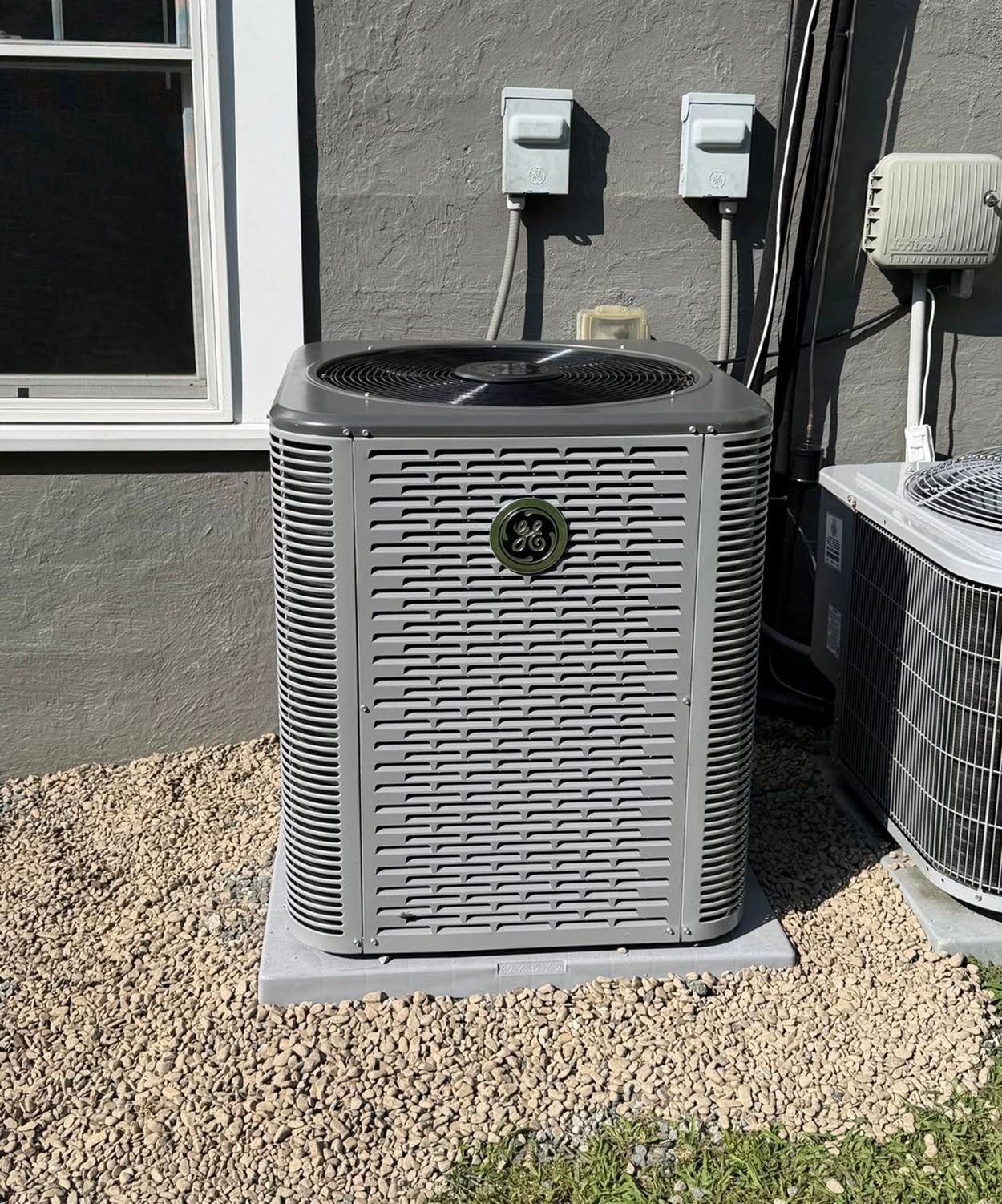 Outdoor air conditioner unit beside a house wall, sitting on gravel.