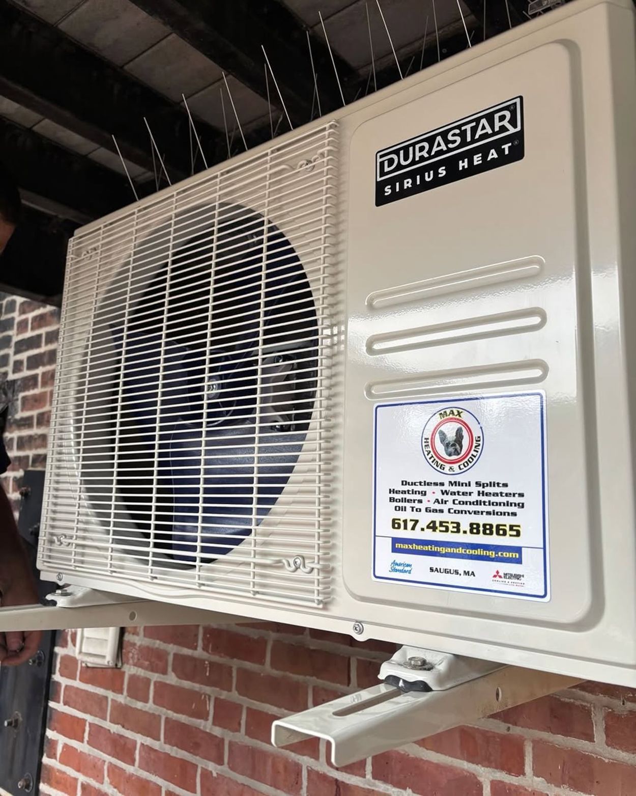 Beige wall-mounted air conditioner unit with a fan and service sticker on a brick exterior wall.
