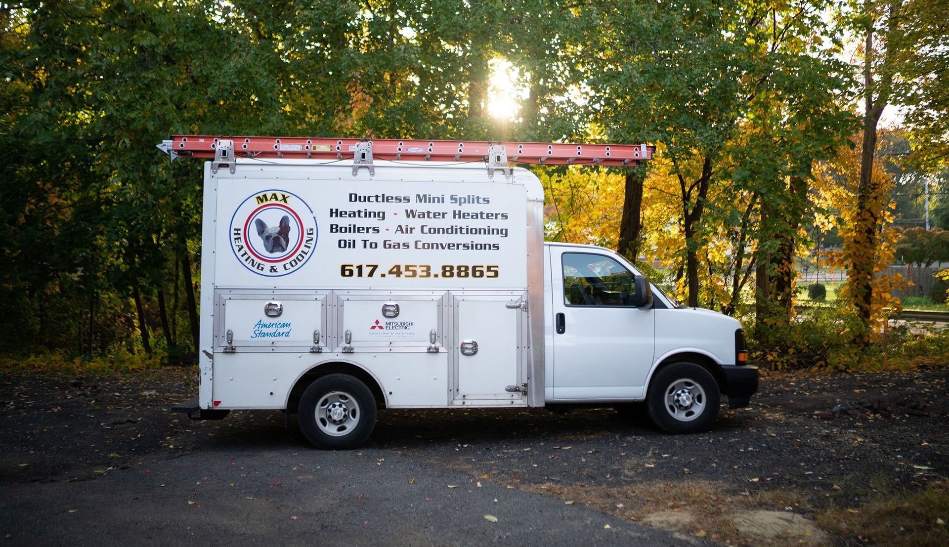 White utility truck with ladder rack and business signage parked on a tree-lined road