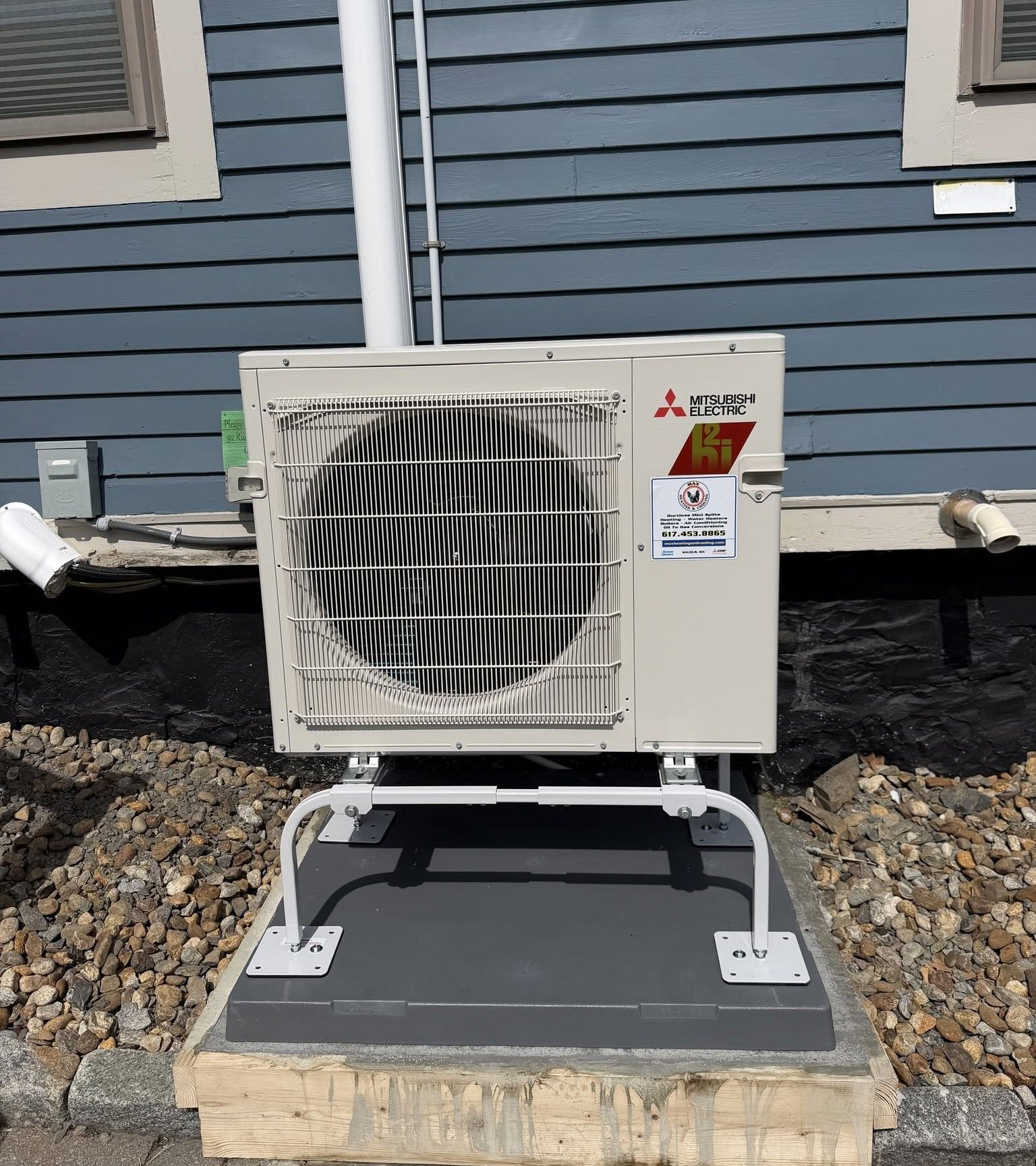 Outdoor Mitsubishi HVAC unit on a white stand beside a house with blue siding.