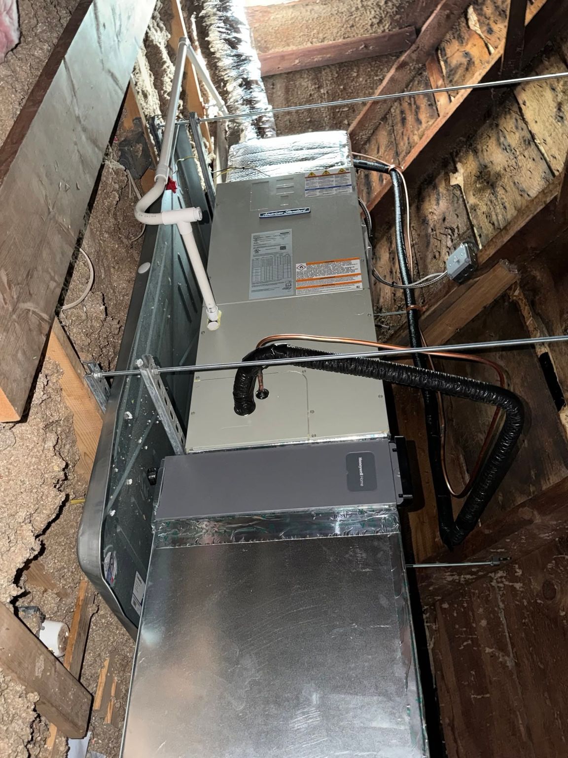 Two HVAC units in a narrow brick utility shaft with pipes and wiring