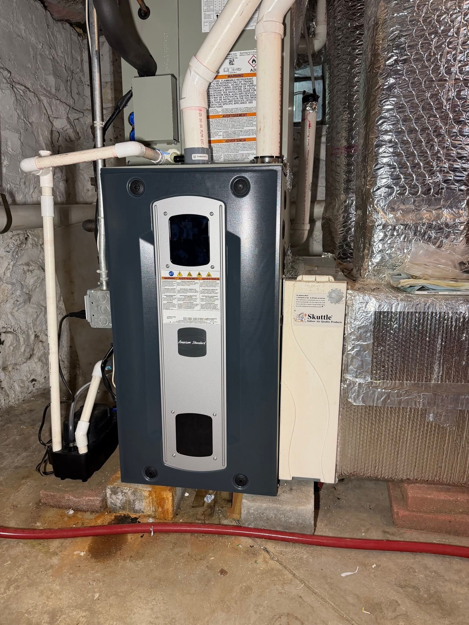 Basement utility area with a black furnace, white pipes, and foil-insulated ductwork behind it.