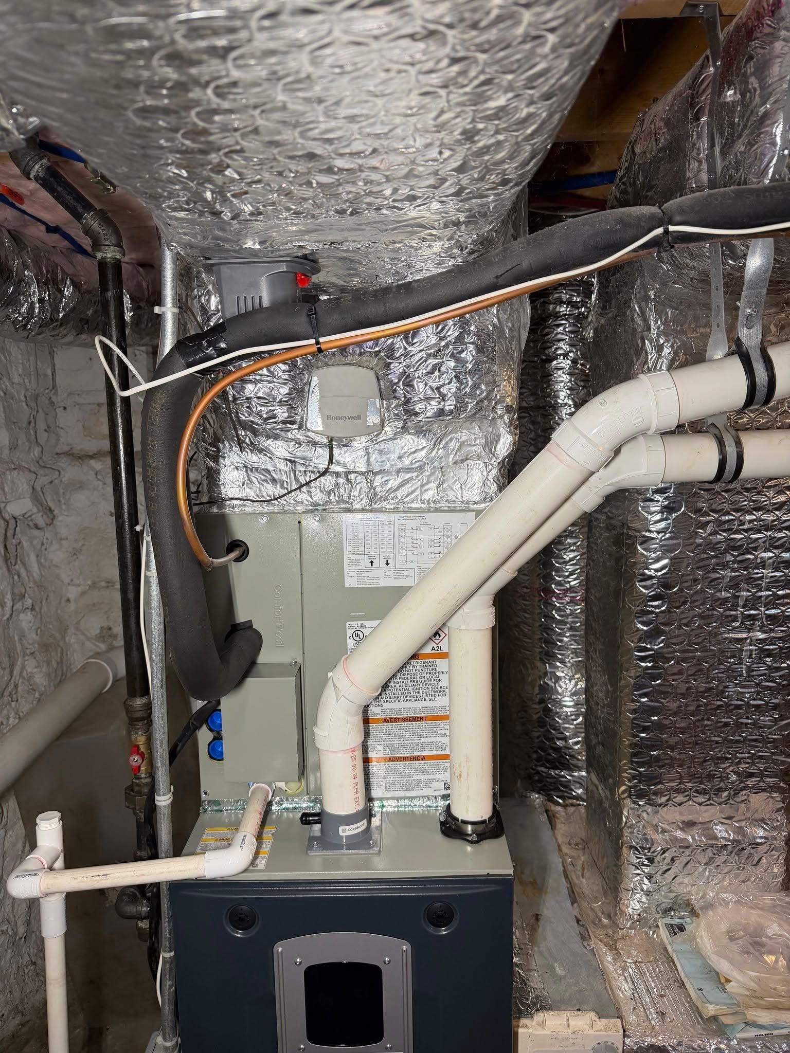 Basement HVAC furnace with white ducts and reflective insulation in a utility room