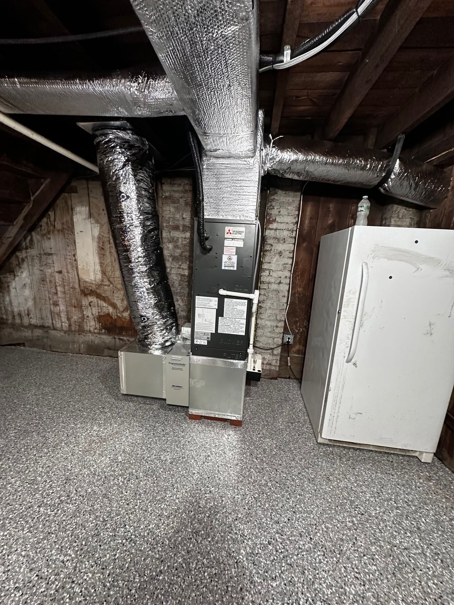 Basement utility room with exposed ducts, furnace, and white cabinet on a speckled floor.