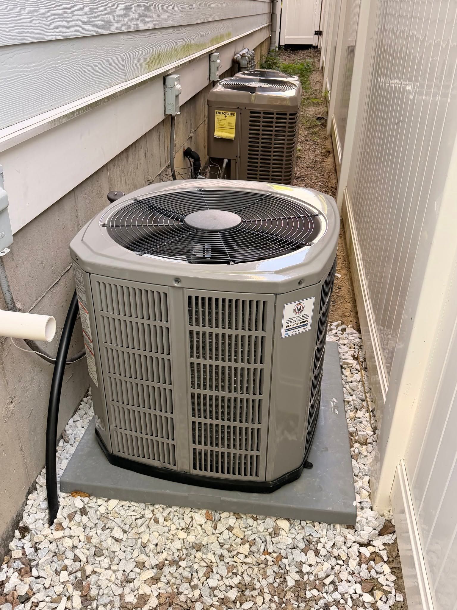 Two outdoor air conditioning units in a narrow side yard between house walls.