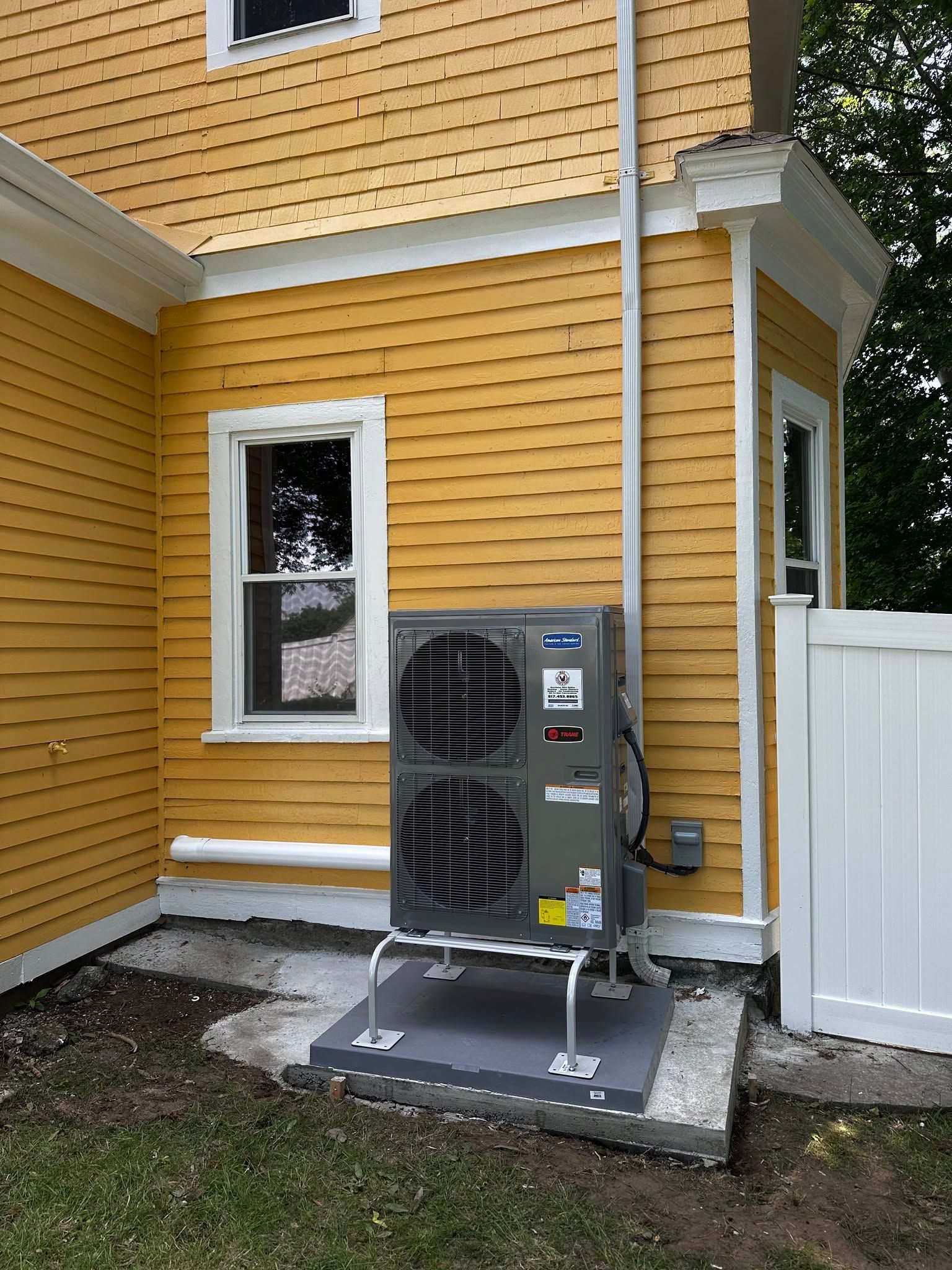 Outdoor HVAC unit beside a yellow house with white trim and a nearby window and fence.