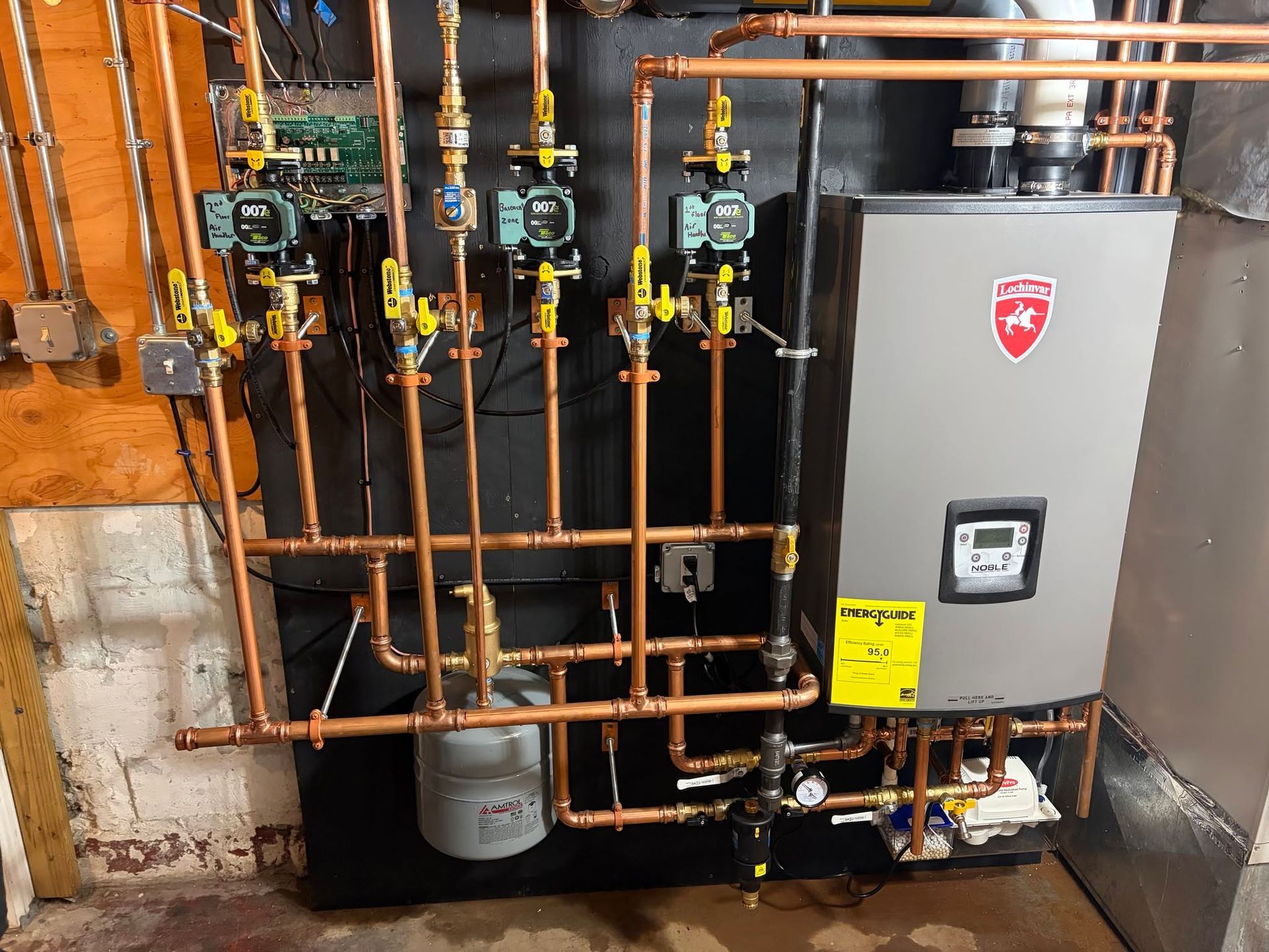 Copper pipes and a gray boiler unit in a utility room against unfinished walls.