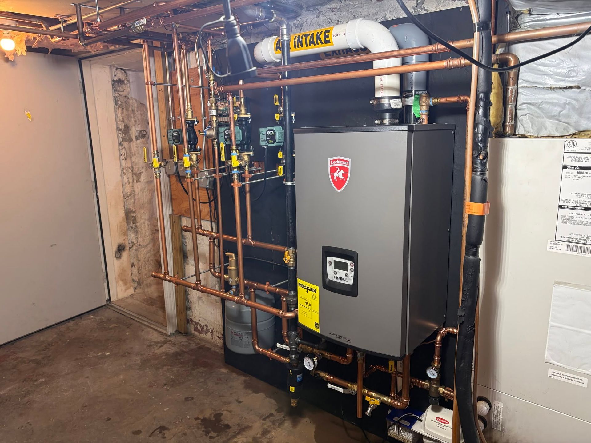 Basement utility room with gray heating equipment and copper pipes against concrete walls.