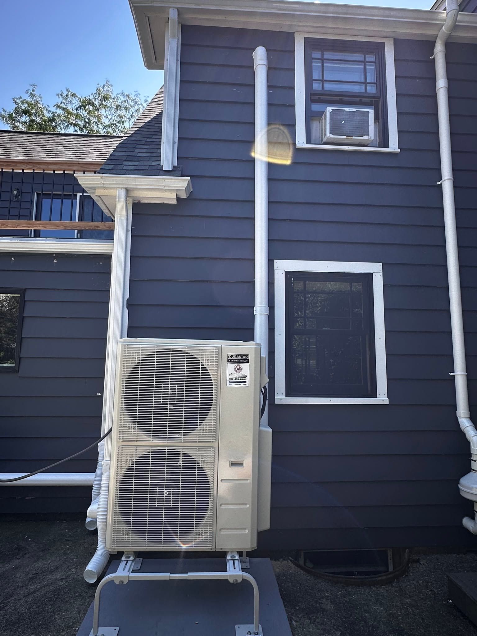 Outdoor air-conditioning unit beside a dark blue house with white trim and a second-story window.