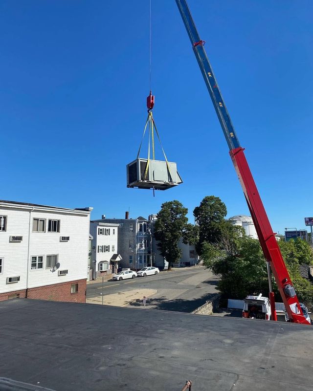 Crane lifting a large white crate over a residential parking lot on a clear day