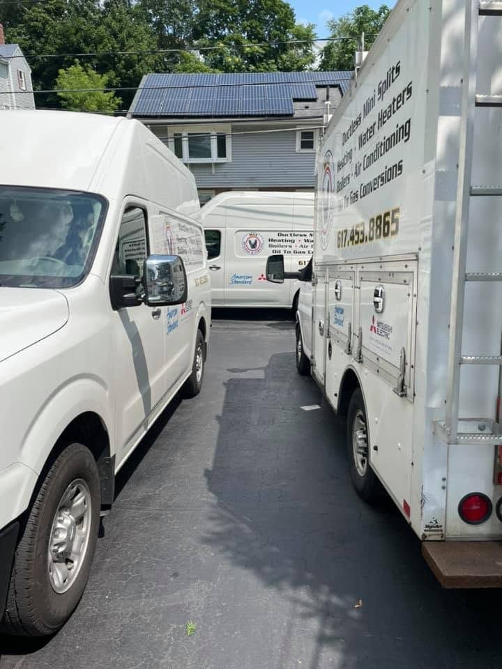 White vans and a box truck parked in a narrow driveway, with a house and solar panels in the background