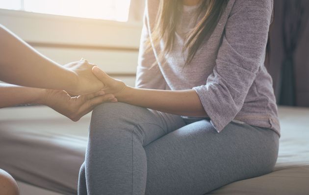 Hands clasped in a comforting gesture on a couch by a bright window