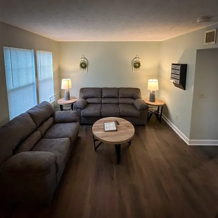 Cozy living room with brown sofas, round coffee table, lamps, and wood flooring
