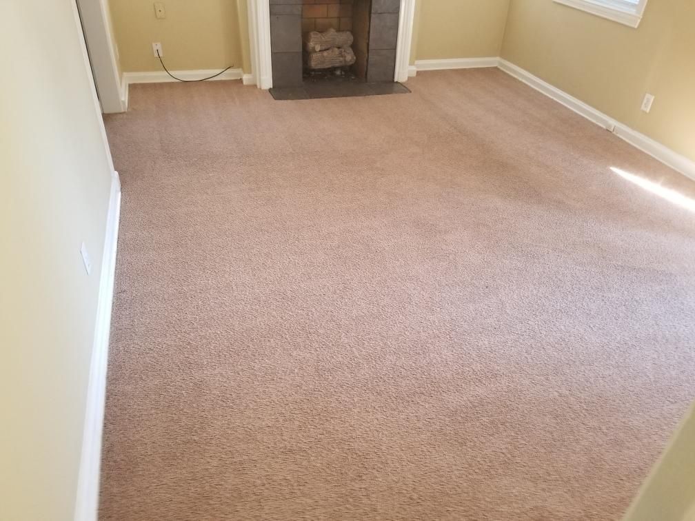 Empty beige carpeted room with tan walls and a fireplace at the far end