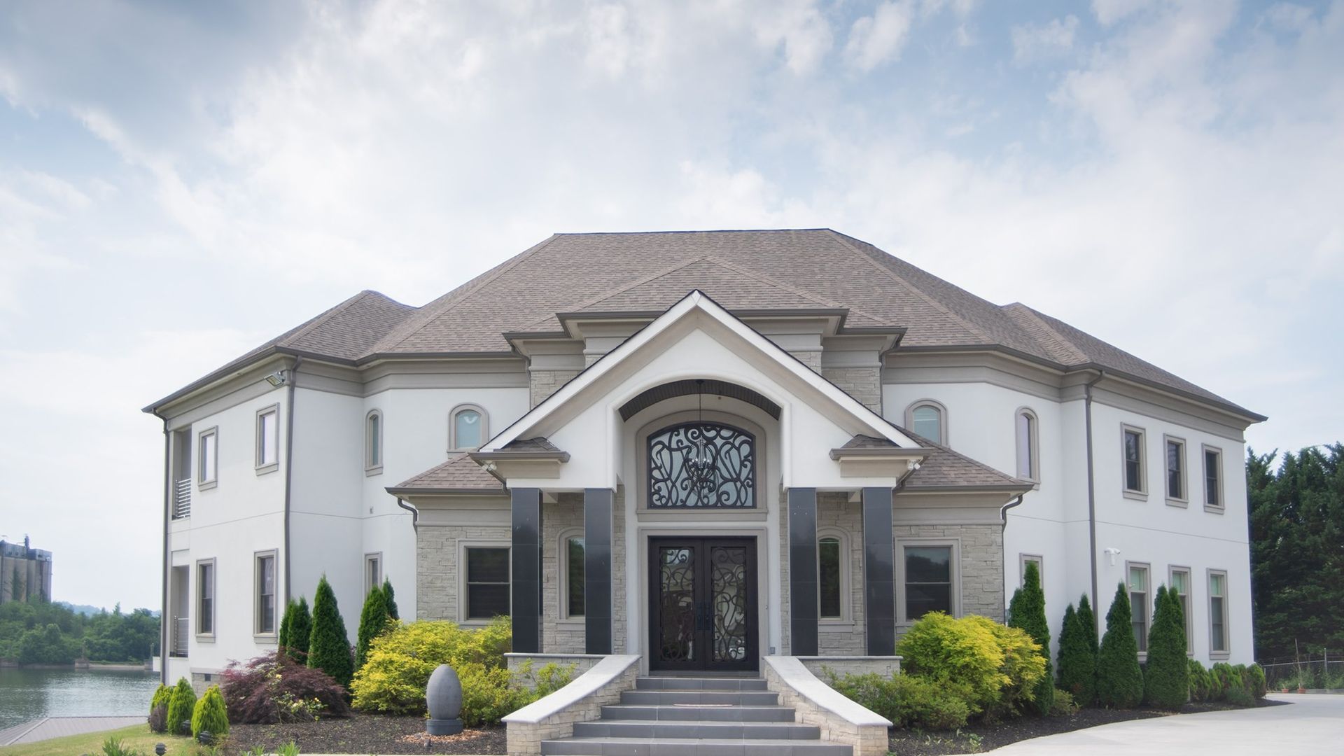 A large white house with a brown roof is sitting next to a body of water.
