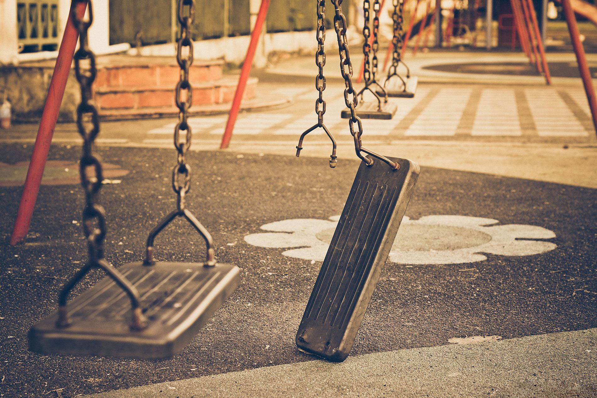 A broken swing is sitting on the ground in a playground.