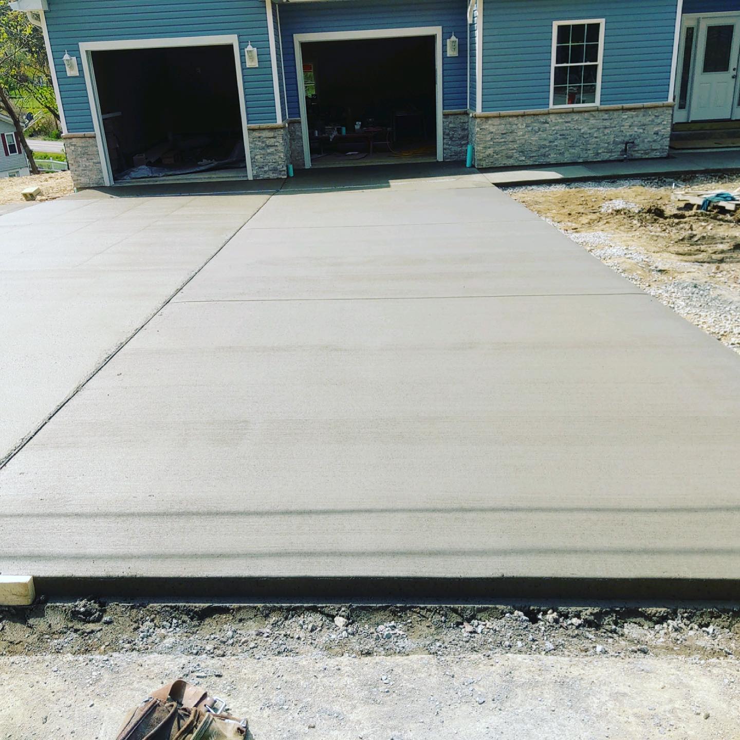 Fresh concrete driveway leading to a blue house with two open garage bays