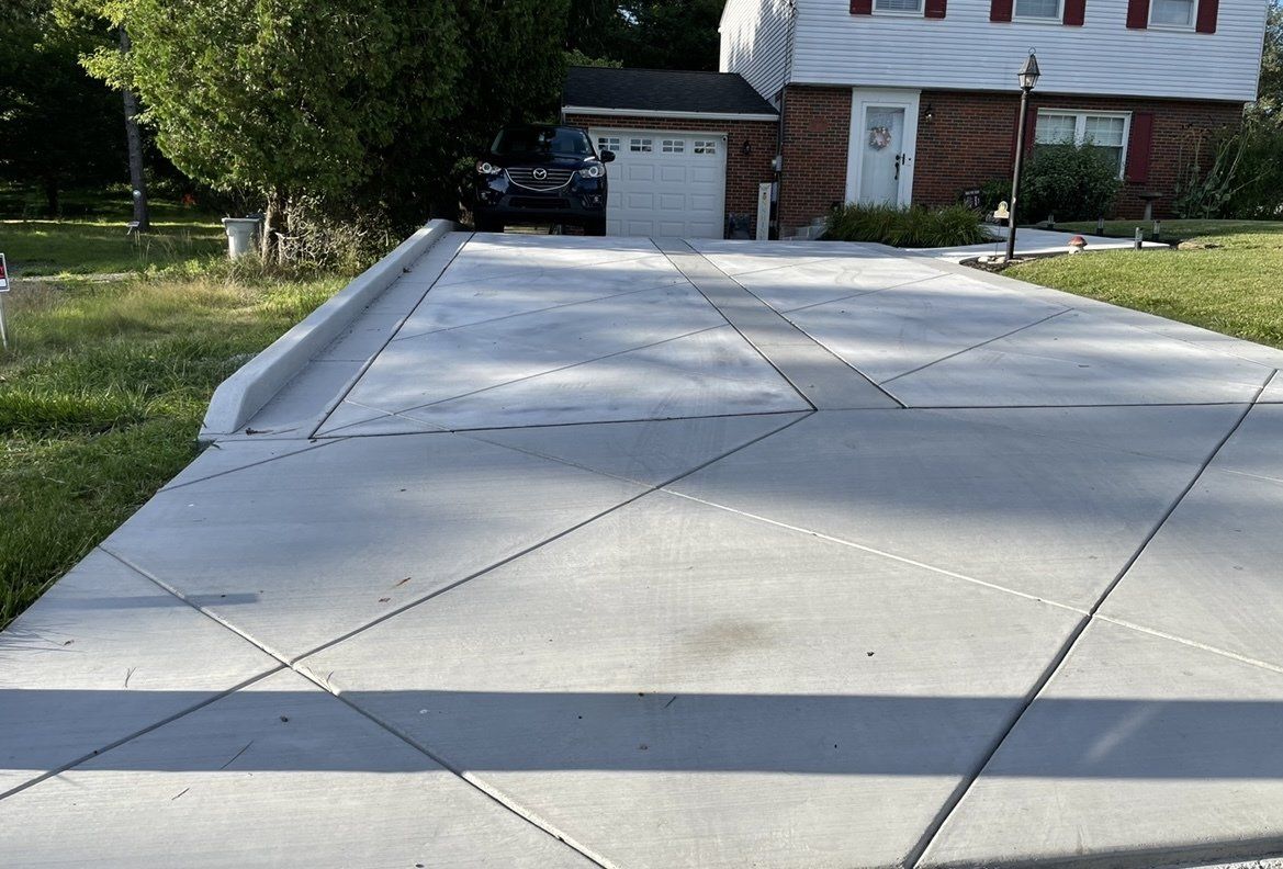 Concrete driveway with expansion joints leading to a house and garage, bordered by grass and trees